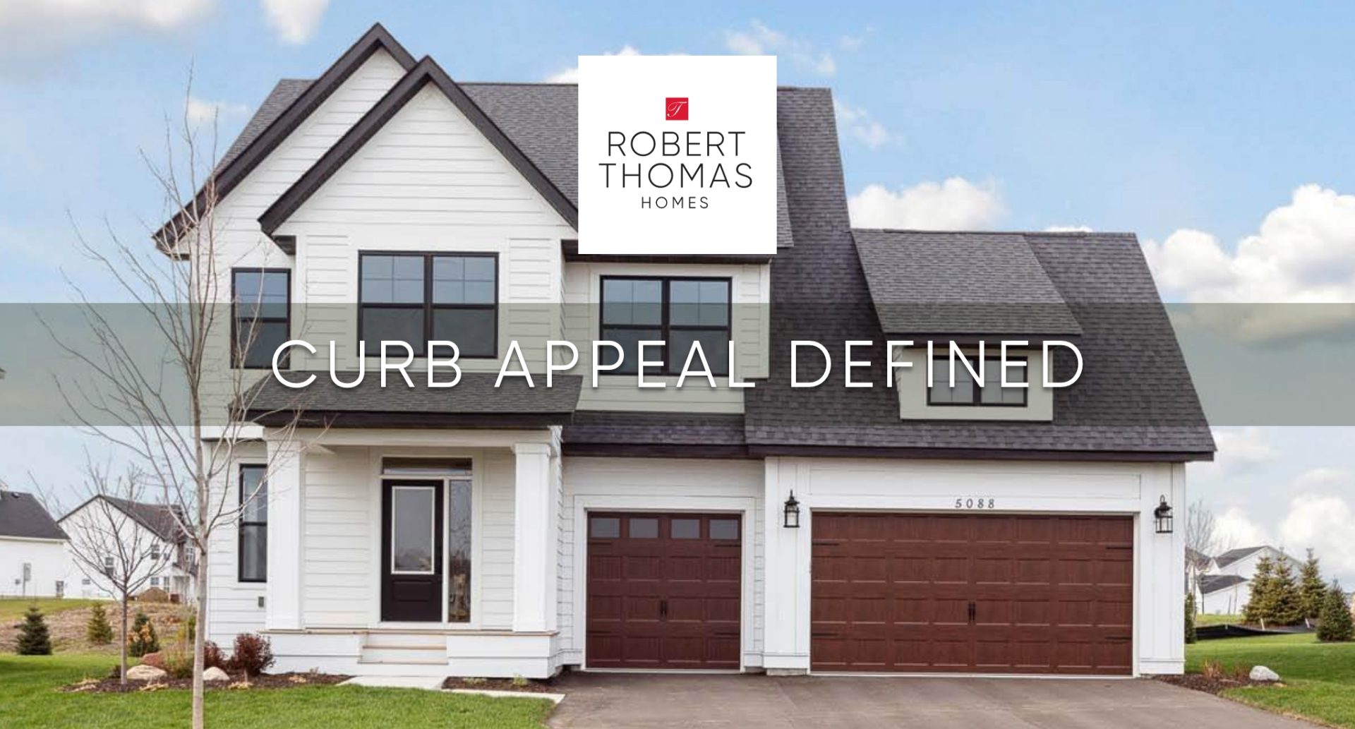 Exterior of a home with white siding and black windows. Grey roof and brown wood-toned garage doors. Gre grass surrounds home.